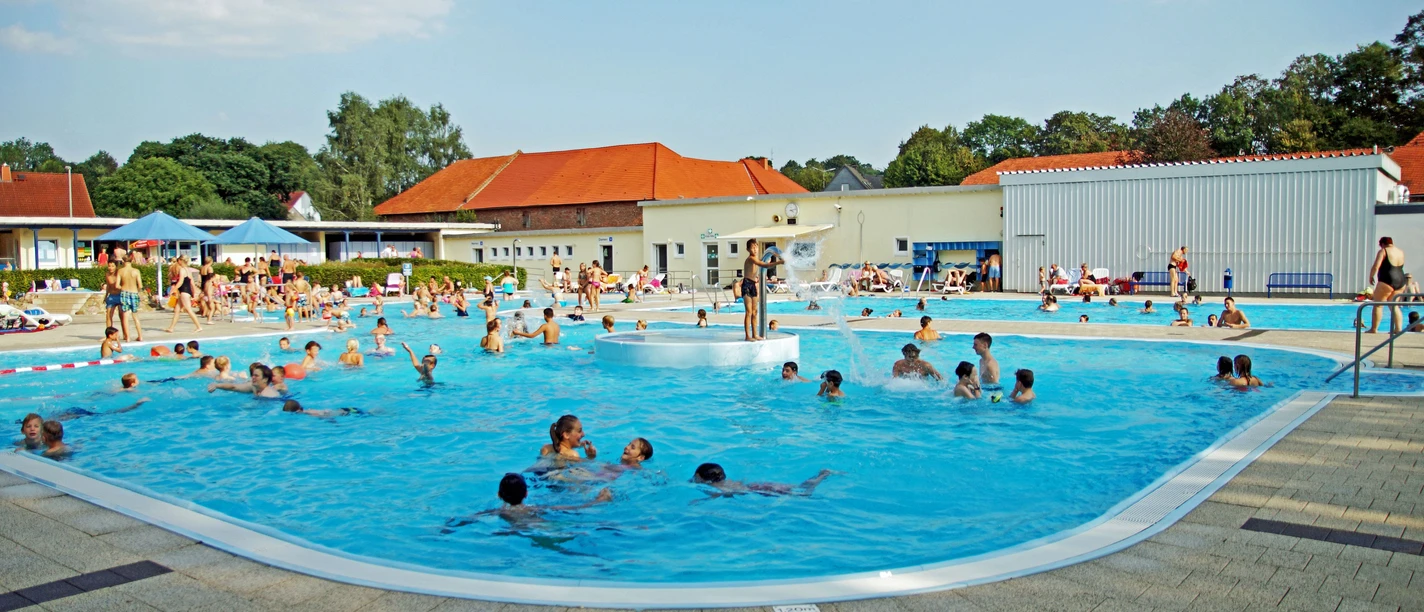 Menschen genießen sommerlichen Badespaß in einem großen Freibad mit verschiedenen Pools.