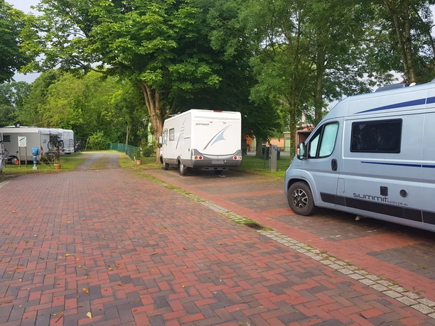 Wohnmobilstellplatz Seglertreff Otterndorf Wohnmobile unter grünen Bäumen auf dem gepflasterten Stellplatz Seglertreff in Otterndorf.