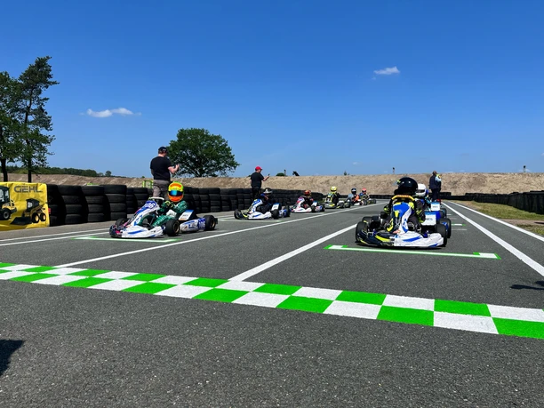 Kartbahn 5.jpg Mehrere Fahrer in Rennkarts warten bei Sonnenschein an der Startlinie einer modernen Kartbahn.