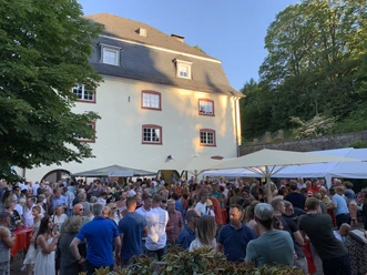 Wein- und Musikfest Menschenmenge feiert ausgelassen im Freien vor einem historischen Gebäude mit gelber Fassade.