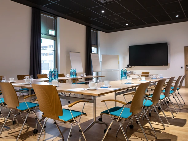 0073.jpg Moderner Konferenzraum mit Holzstühlen, Tischen in U-Form, Flipcharts und großem Bildschirm.