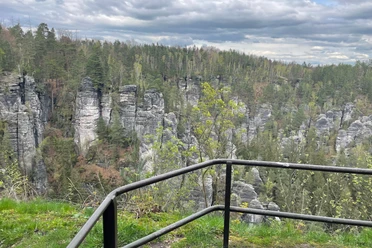 Wehlstein view View of a wooded rocky landscape with gray cliffs and green trees, a black railing in the foreground; cloudy sky.