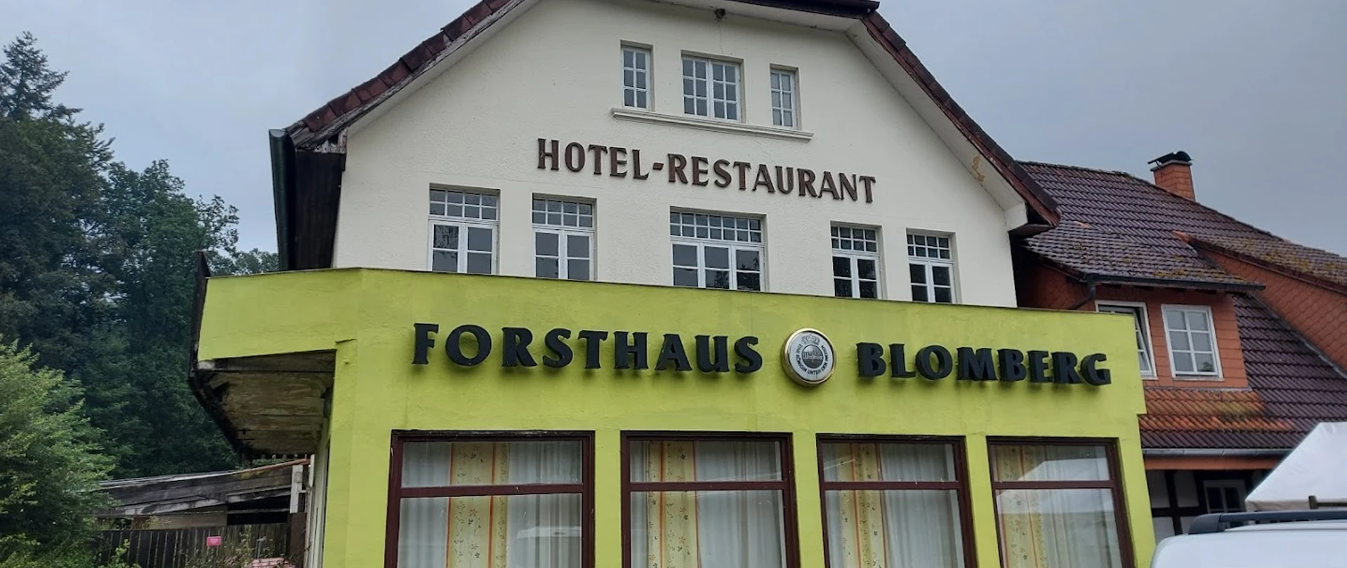 Cafe Forsthaus vor bewölktem Himmel, Teil eines Hotel-Restaurants in einem zweistöckigen Gebäude.