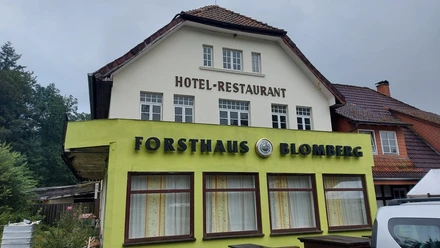 Cafe Forsthaus Cafe Forsthaus vor bewölktem Himmel, Teil eines Hotel-Restaurants in einem zweistöckigen Gebäude.