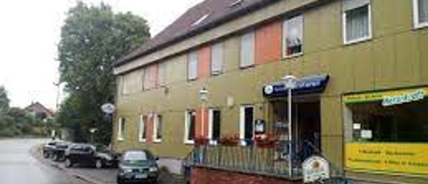 Gaststätte Wittelmeyer Die Gaststätte Wittelmeyer mit grün-gelblichen Fassaden und orangefarbenen Markisen an den Fenstern.