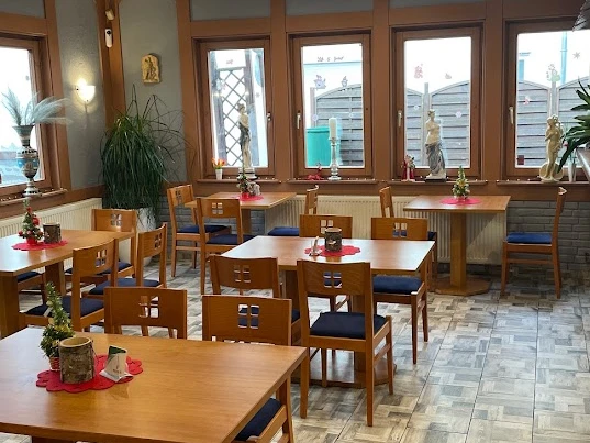 Greek House Grill Restaurant mit Holzmöbeln, dekorativen Pflanzen und großen Fenstern, die viel Tageslicht einlassen.