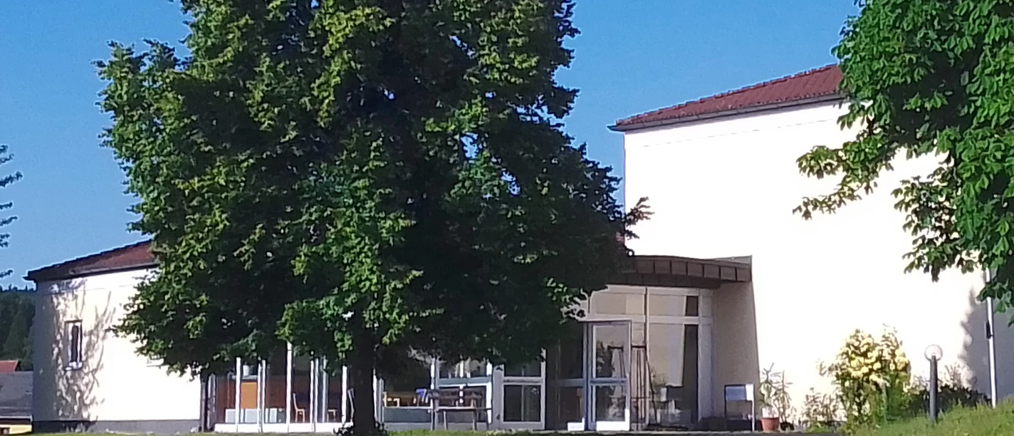 A modern building with large windows, surrounded by green trees and lawns, under a clear blue sky.