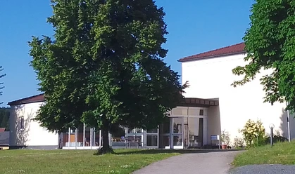 Sport-und Freizeittreff Reinhardtsdorf-Schöna Een modern gebouw met grote ramen, omringd door groene bomen en gazons, onder een strakblauwe hemel.