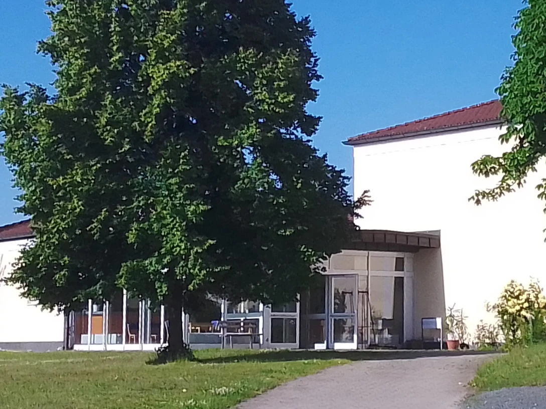 Sport-und Freizeittreff Reinhardtsdorf-Schöna Ein modernes Gebäude mit großen Fenstern, umgeben von grünen Bäumen und Rasen, unter einem klaren blauen Himmel.A modern building with large windows, surrounded by green trees and lawns, under a clear blue sky.Moderní budova s velkými okny, obklopená zelenými stromy a trávníky, pod jasně modrou oblohou.Nowoczesny budynek z dużymi oknami, otoczony zielonymi drzewami i trawnikami, pod czystym, błękitnym niebem.Een modern gebouw met grote ramen, omringd door groene bomen en gazons, onder een strakblauwe hemel.Un edificio moderno con grandi finestre, circondato da alberi e prati verdi, sotto un cielo azzurro e limpido.