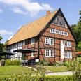 blomberger hof-1 Fachwerkhaus mit roten Ziegeln und großem Satteldach, umgeben von grüner Landschaft und Sonnenschirmen.