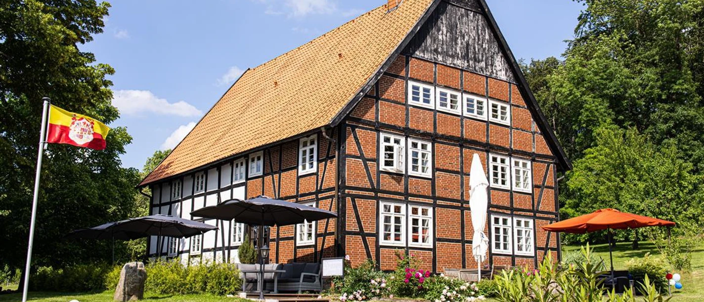 blomberger hof-1 Fachwerkhaus mit roten Ziegeln und großem Satteldach, umgeben von grüner Landschaft und Sonnenschirmen.