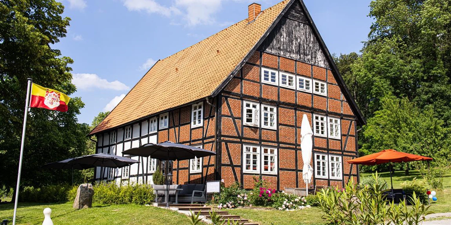 blomberger hof-1 Fachwerkhaus mit roten Ziegeln und großem Satteldach, umgeben von grüner Landschaft und Sonnenschirmen.