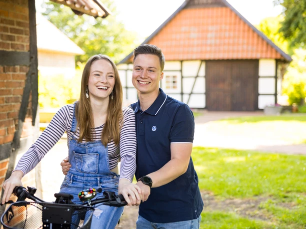 Alte Scheune & historische Schmiede Holzhausen II. Ein junges Paar lacht fröhlich vor einer Fachwerkscheune an einem sonnigen Tag.