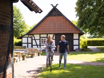 Alte Scheune & historische Schmiede Holzhausen II. Ein Fachwerkgebäude in Holzhausen mit Spaziergängern und Bänken im einladenden Vorgarten.