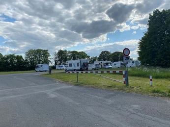 Festwiese Nienburg Wohnmobile stehen auf einer asphaltierten Fläche zwischen Bäumen unter einem bewölkten Himmel.