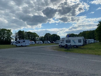 Parkplatz mit Wohnmobilen unter teils bewölktem Himmel; umgeben von Bäumen auf der Festwiese Nienburg.