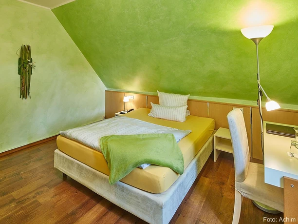 Ein gemütliches Schlafzimmer mit einer grünen Wandfarbe und einem großen Bett. Neben dem Bett befindet sich ein Schreibtisch und eine Lampe.