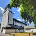 Weiße Kirche mit grünem Turm, flankiert von Bäumen, unter wolkenlosem, blauem Himmel in Hövelhof.