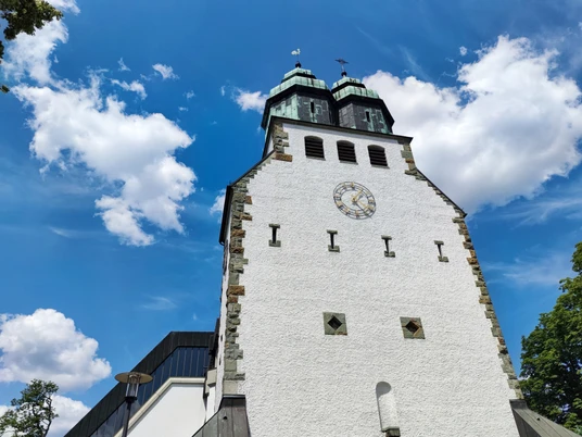Katholische Kirche St. Johannes Nepomuk Der weiße Kirchturm der Katholischen Kirche St. Johannes Nepomuk ragt vor einem blauen Himmel empor.