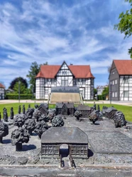 Geländemodell Schlossgarten Bronzeplastik eines Schlossgartens vor einem Fachwerkhaus unter blauem Himmel mit weißen Wolken.