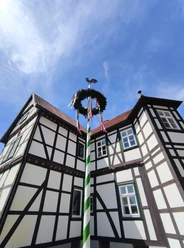 Fachwerk-Jagdschloss in Hövelhof mit einem festlich geschmückten Maibaum, der den blauen Himmel ziert.