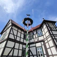 Fachwerk-Jagdschloss in Hövelhof mit einem festlich geschmückten Maibaum, der den blauen Himmel ziert.