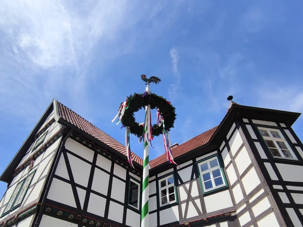 Fachwerk-Jagdschloss in Hövelhof mit einem festlich geschmückten Maibaum, der den blauen Himmel ziert.