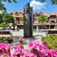 Glockenspiel am Hövelmarktplatz mit blühenden rosa Blumen im Vordergrund und einem modernen Brunnen.
