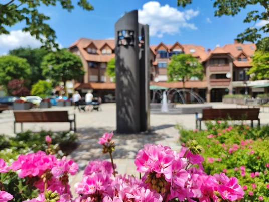 Glockenspiel auf dem Hövelmarktplatz Glockenspiel am Hövelmarktplatz mit blühenden rosa Blumen im Vordergrund und einem modernen Brunnen.