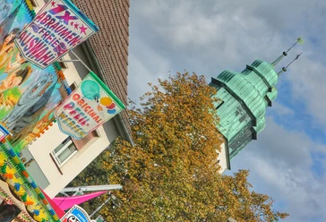 Hövelmarkt Buntes Marktgeschehen mit geschmückten Ständen und historischem Turm im Hintergrund bei bewölktem Himmel.