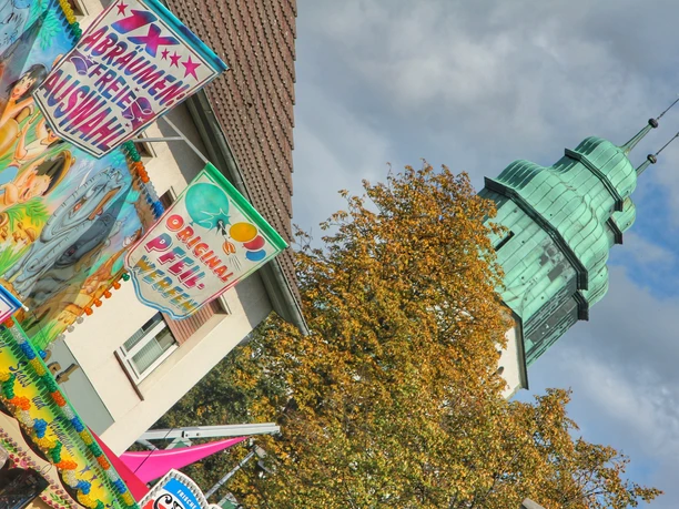 Hövelmarkt Buntes Marktgeschehen mit geschmückten Ständen und historischem Turm im Hintergrund bei bewölktem Himmel.