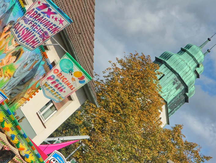 Hövelmarkt Buntes Marktgeschehen mit geschmückten Ständen und historischem Turm im Hintergrund bei bewölktem Himmel.