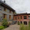 Spinnerei Historisches Gebäude mit Schieferfassade, modernem Anbau und „Spinnerei“-Schriftzug im Grünen.