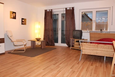 IMG_1145.JPG Ein helles Wohnzimmer mit Holzboden, gemütlicher Sitzecke, dezenter Beleuchtung und großen Fenstern.