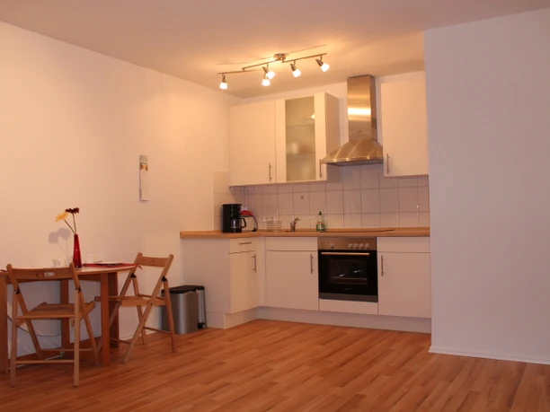 IMG_1148.JPG Moderne, minimalistisch eingerichtete Küche mit Holzfußboden, weißen Schränken und kleinem Tischset.