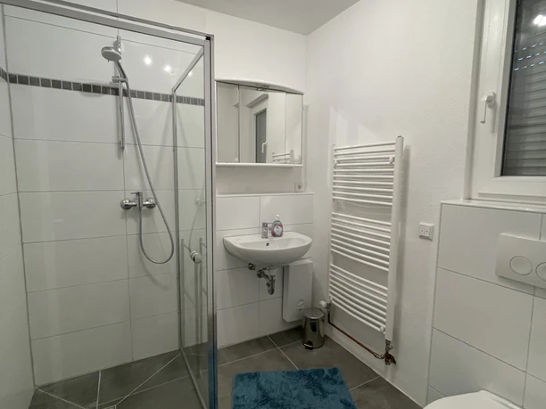 FeWoFachwerkBad.JPG Modernes, helles Badezimmer mit Duschkabine, Waschbecken, WC und Heizkörper auf grauem Fliesenboden.