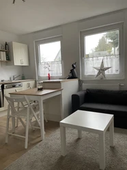 Gemütlicher Wohnbereich mit Küchenzeile, Esstisch und Sofa. Helle Fensterfront mit dekorativem Stern.