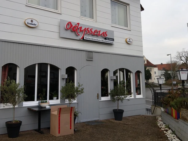 Außenansicht des griechischen Restaurants Odysseus by Nikos mit grauer Fassade und roten Lettern