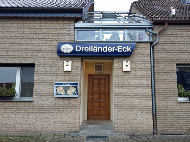 Eingang der Gaststätte Dreiländer-Eck mit blauem Schild an einer hellen Backsteinfassade