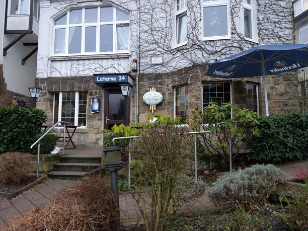 Eingang der Bar Laterne 34 mit Steinfront, Pflanzen und blauem Sonnenschirm