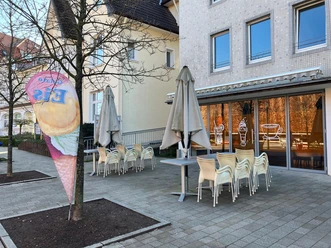 Eiscafé Therme: Außenbereich mit gestapelten Stühlen, Sonnenschirmen und Eisfahne