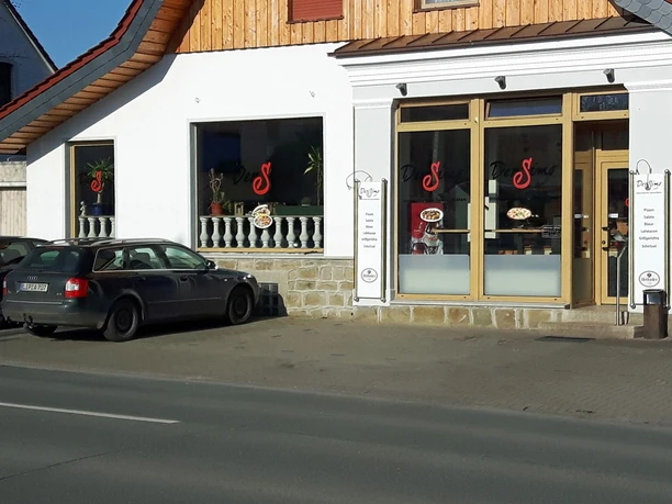 Restaurant Der Simo mit großen Fenstern, Speisekarten und geparktem Auto an der Straße