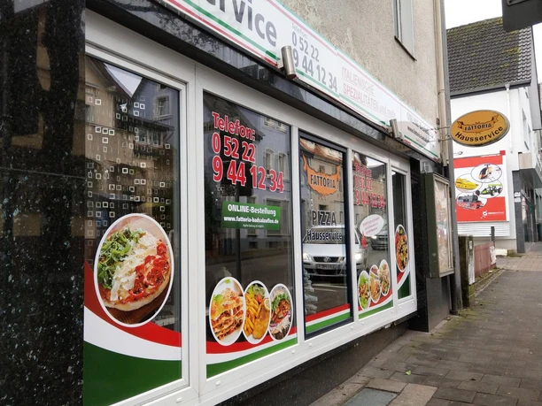 Fattoria Pizza quer Schaufenster der Pizzeria Fattoria mit Pizzafotos und Lieferservice-Hinweis an der Straße