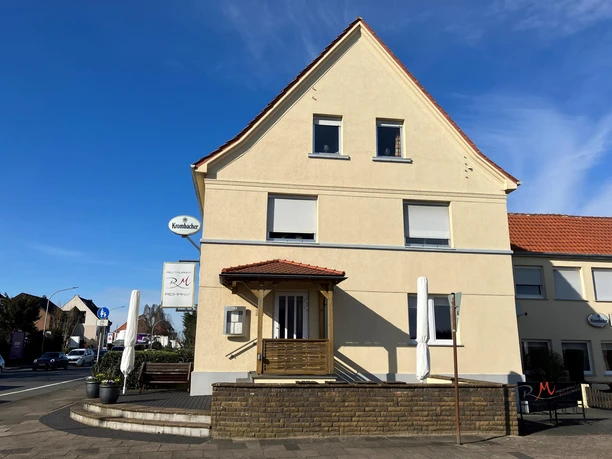 ReiMans Restaurant in hellem Gebäude mit Eingang, Terrasse und Schildern bei Sonnenschein