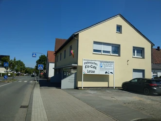 Gelbes Gebäude des Eis-Café Lerose mit Eistüte an der Fassade und Parkplatz an der Straße
