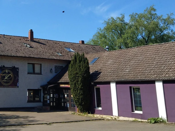 Außenansicht der Diwan Lounge mit violetter Fassade, Schild und großem Baum