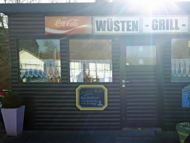Wüsten-Grill Fassade des Wüsten-Grills mit großem Schild, Fenstern und starker Sonneneinstrahlung