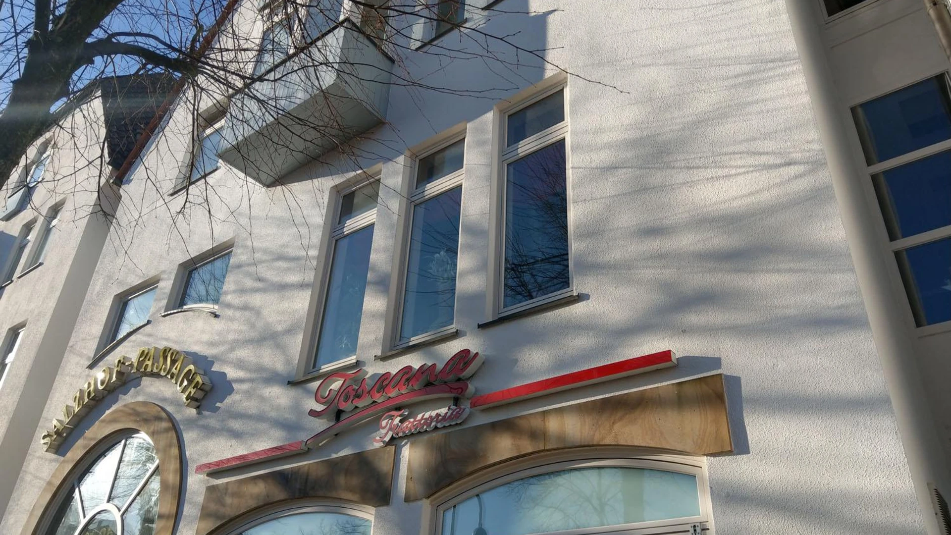 Fassade der Trattoria Toscana mit Fenstern und Baumästen im Sonnenlicht