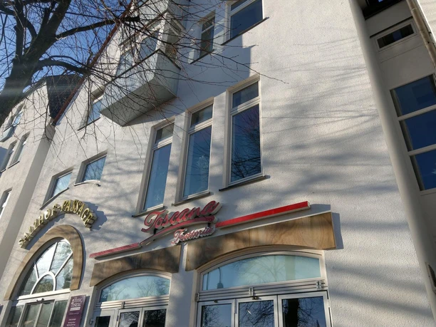 Fassade der Trattoria Toscana mit Fenstern und Baumästen im Sonnenlicht