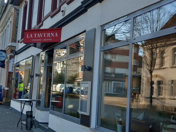 Außenansicht des Restaurants La Taverna mit rotem Schild und großen Schaufenstern